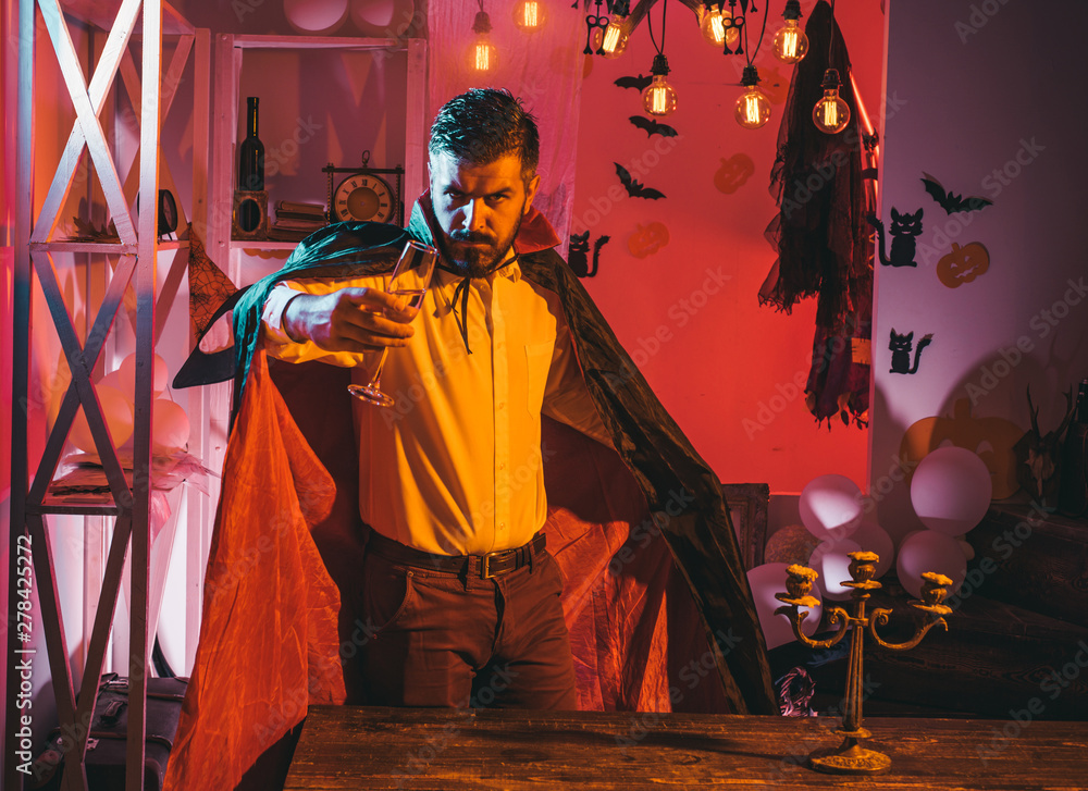 Fototapeta premium Halloween party. Magician drinks sparkling wine. Attractive bearded man in black magical coat. Halloween holiday concept.