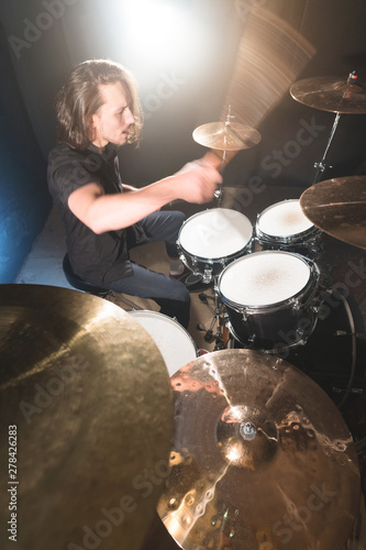 Portrait of a long-haired drummer with chopsticks in his hands sitting behind a drum set. Low key. Concepts of the creative freedom of the millenial generation