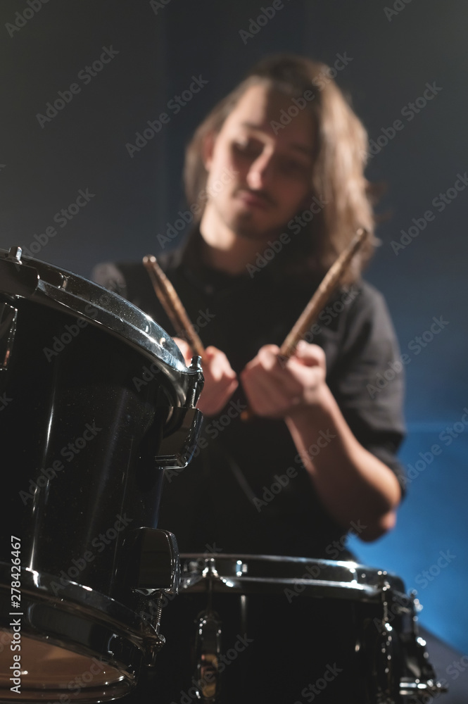 Fototapeta premium Close-up detail of a drum set against a blurred out-of-focus drummer with drum sticks