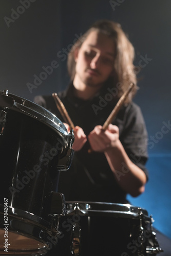 Close-up detail of a drum set against a blurred out-of-focus drummer with drum sticks