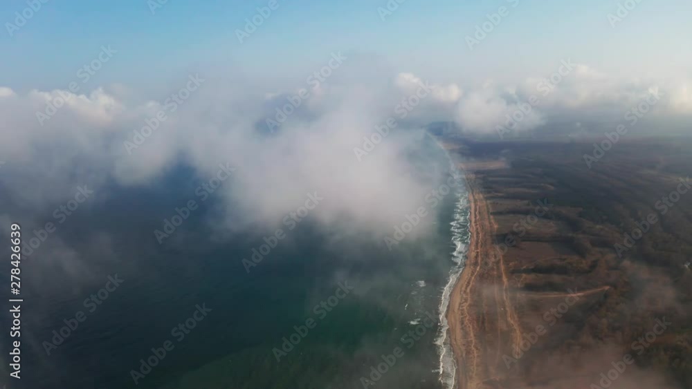 Scenic aerial view through moving white clouds on coastline and sea surface. The drone slide turn flies forward high in the blue sky through the fluffy clouds on the panorama of the sea shore. Scenic aerial view through moving white clouds on coastline and sea surface. The drone slide turn flies forward high in the blue sky through the fluffy clouds on the panorama of the sea shore.