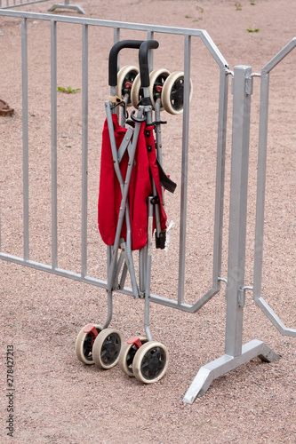 Folding stroller for children in red, standing at the fence photo