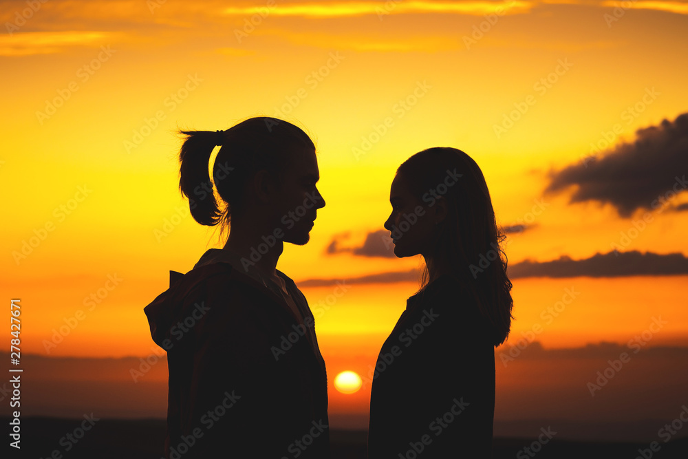 Waist silhouettes of a young millenial couple in love with a man and a girl look at each other. Two profile of a young couple at sunset