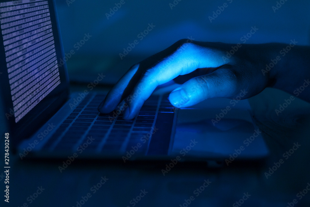 Foto A computer programmer or hacker prints a code on a laptop keyboard to break into a secret organization system