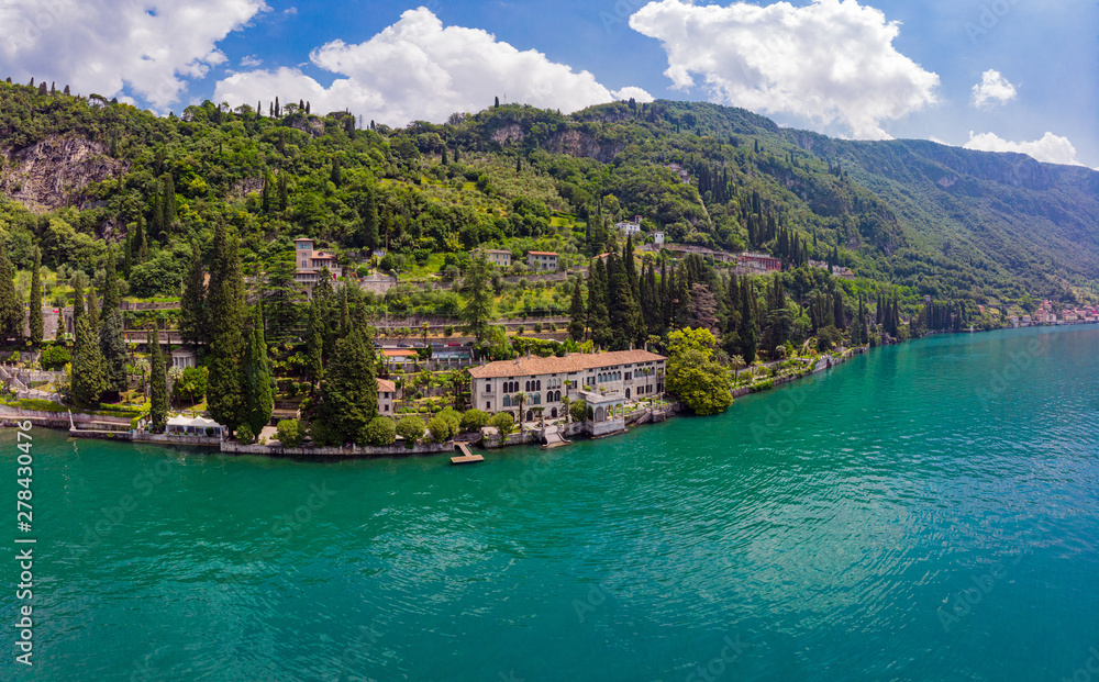 Beautifull aerial panoramic view from the drone to Varenna famous old Italy town on bank of Como lake. High top view to villa Monastero landscape, green hills, mountains and city in sunny summer day