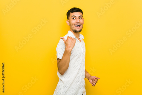 Young hispanic man points with thumb finger away, laughing and carefree.