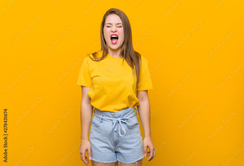 Young woman teenager wearing a yellow shirt screaming very angry and aggressive. Young woman teenager wearing a yellow shirt screaming very angry and aggressive.