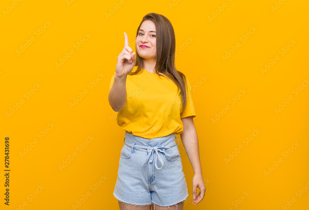 Young woman teenager wearing a yellow shirt showing number one with finger. Young woman teenager wearing a yellow shirt showing number one with finger.