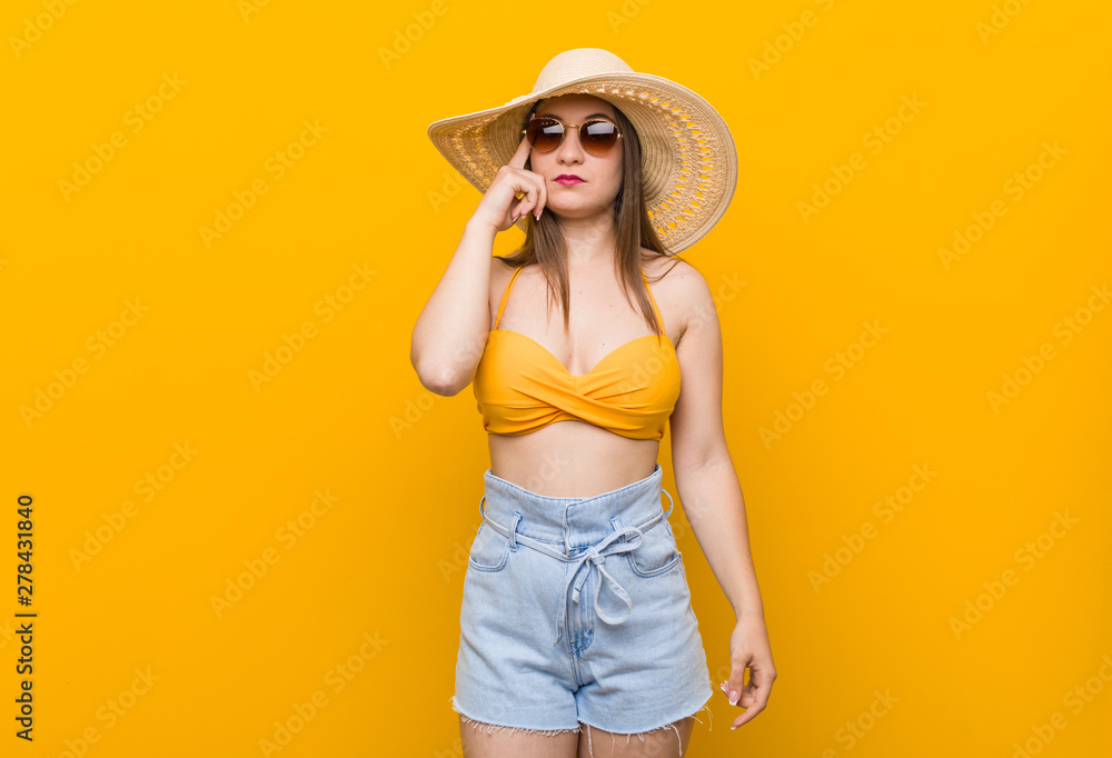 Young caucasian woman wearing a straw hat, summer look pointing temple with finger, thinking, focused on a task. Young caucasian woman wearing a straw hat, summer look pointing temple with finger, thinking, focused on a task.