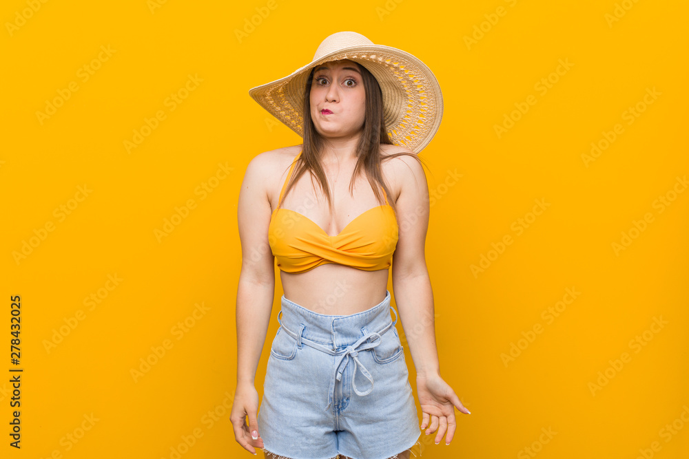 Young caucasian woman wearing a straw hat, summer look shrugs shoulders and open eyes confused. Young caucasian woman wearing a straw hat, summer look shrugs shoulders and open eyes confused.