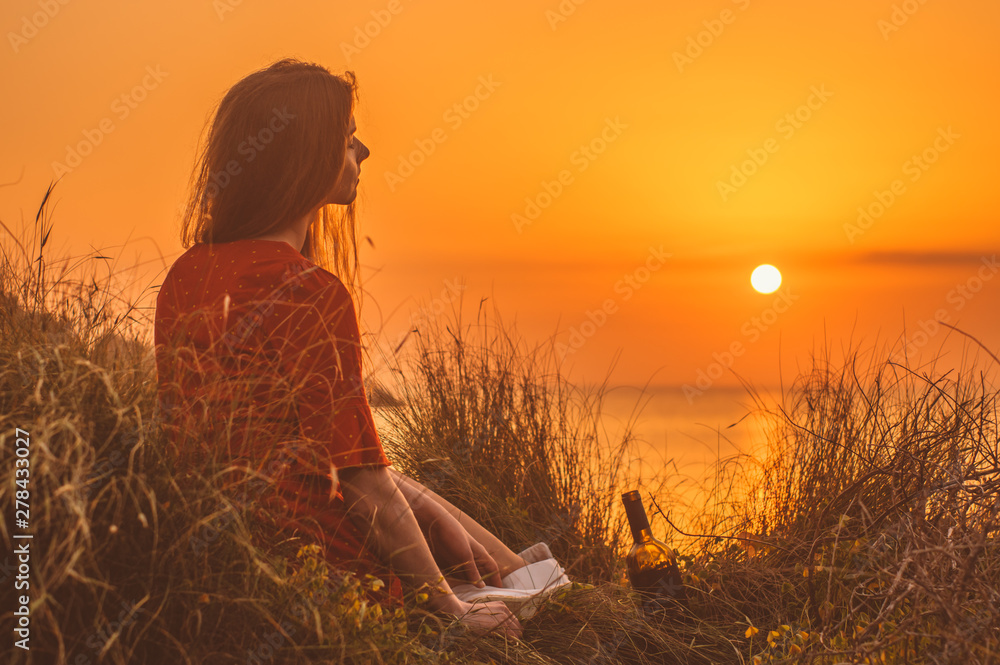 Young blonde girl in red dress sitting in the evening on the beach