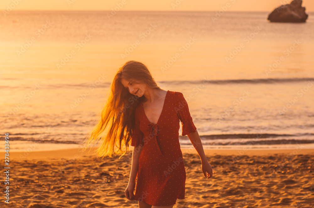 Young blonde girl in red dress walking in the evening on the beach Young blonde girl in red dress walking in the evening on the beach