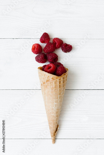 Cuadro en lienzo Cascade of fresh raspberries in a waffle cone of ice cream on a white background