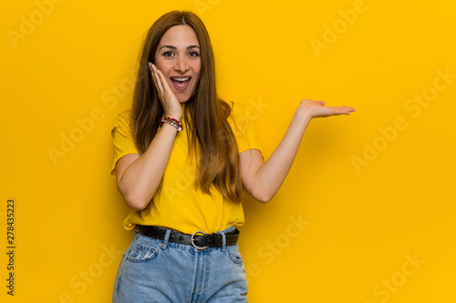 Young ginger redhead woman holds copy space on a palm, keep hand over cheek. Amazed and delighted.