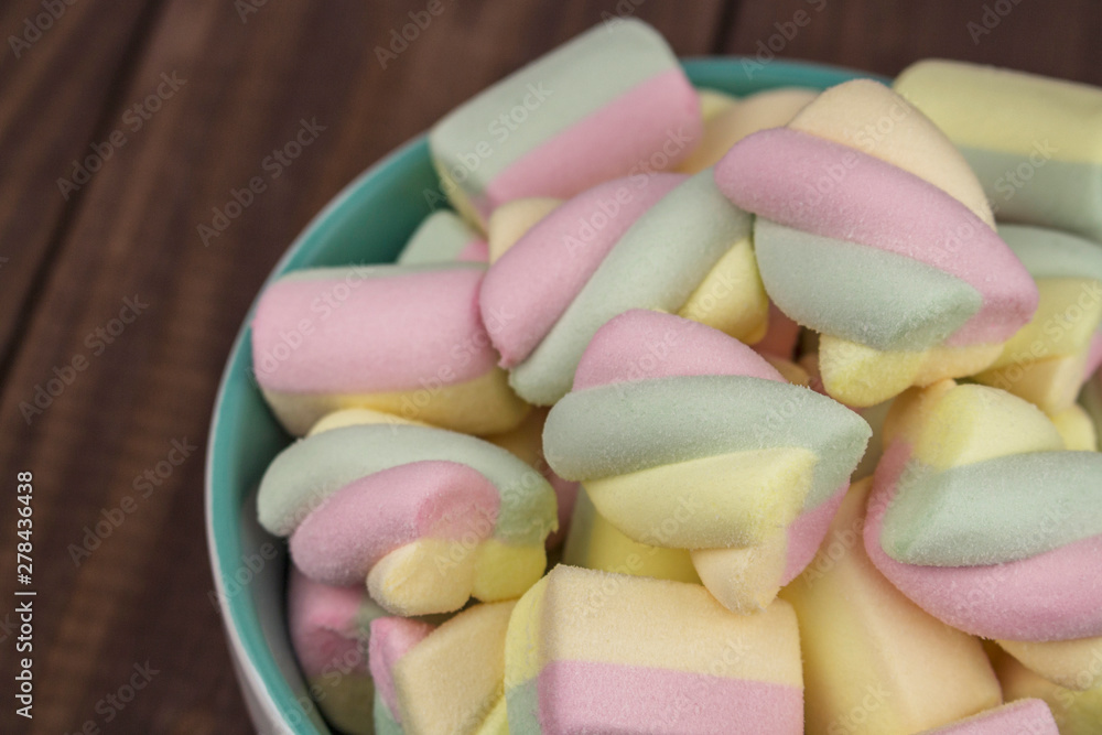 Multicolor spiral marshmallows bowl on wooden table, close-up background. Sweet airy dessert, spiral shape, color yellow pink green blue. Multicolor spiral marshmallows bowl on wooden table, close-up background. Sweet airy dessert, spiral shape, color yellow pink green blue.