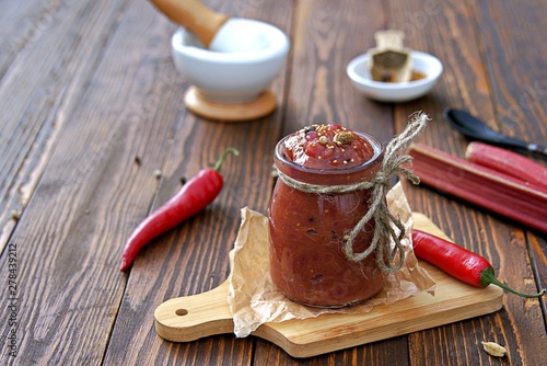 Spicy rhubarb chutney sauce in a glass jar on a wooden background. Preserving, harvesting. Indian food. photo