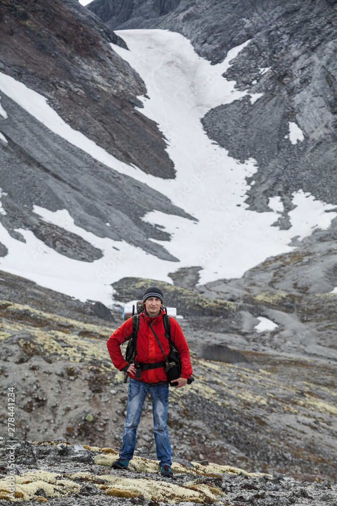 Young Caucasian man with backpack standing against snowy mountain pass, hiking
