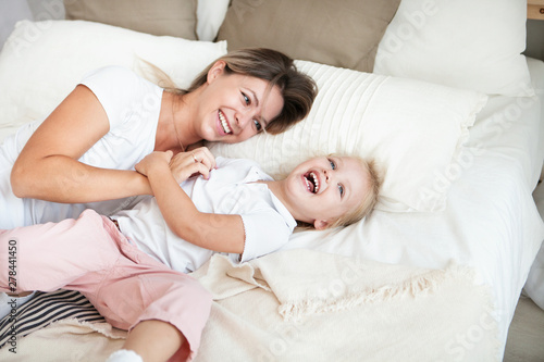 Happy mother and her daughter child girl playing and hugging in bedroom.