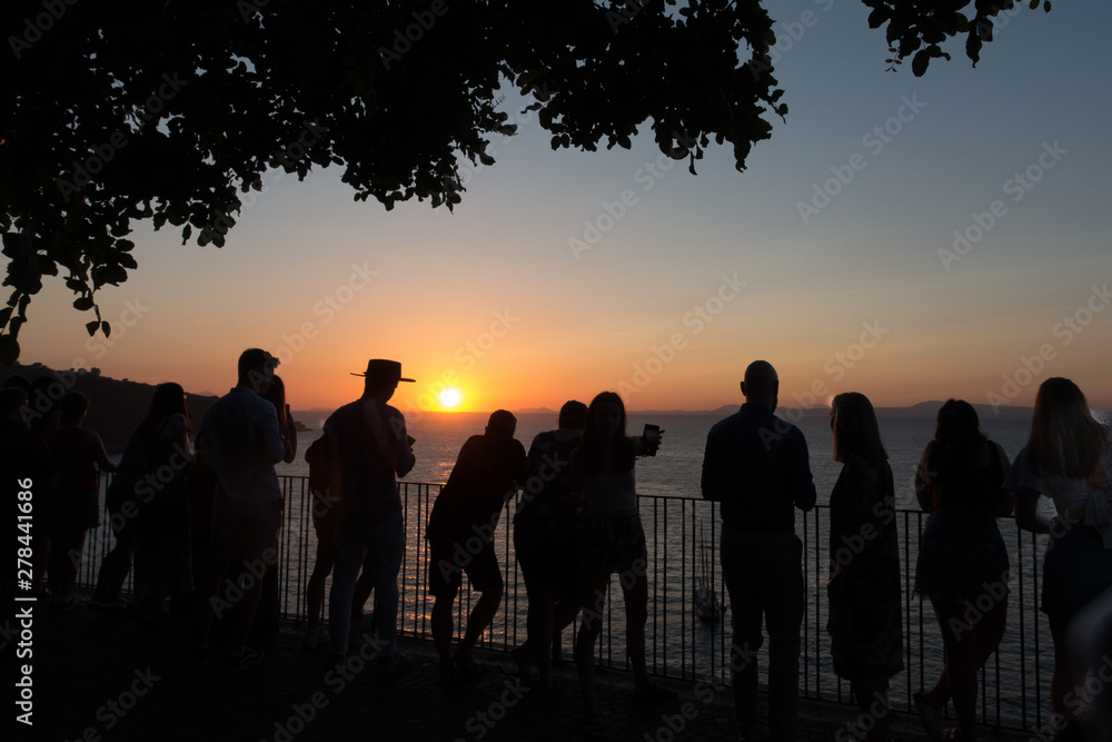 Tourists stand by railings at a viewpoint in Sorrento on the Amalfi coast admiring the sun setting over the sea.Romantic location - Image