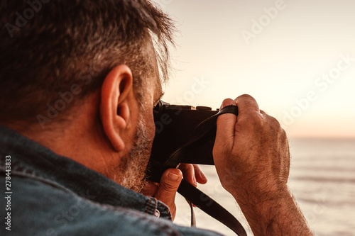 Mann im seitlichen Profil  mit Kamera in der Hand fotografiert das Meer  photo