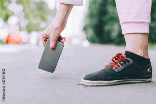 Young woman picks up from the asphalt fallen not crashed smartphone.