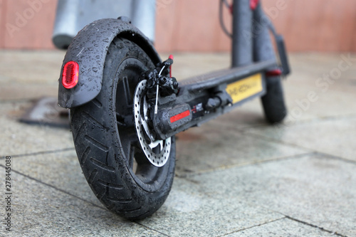 Electric scooter on a parking lot during a rain, water drops on a wheels. City bike rental system, rainy weather