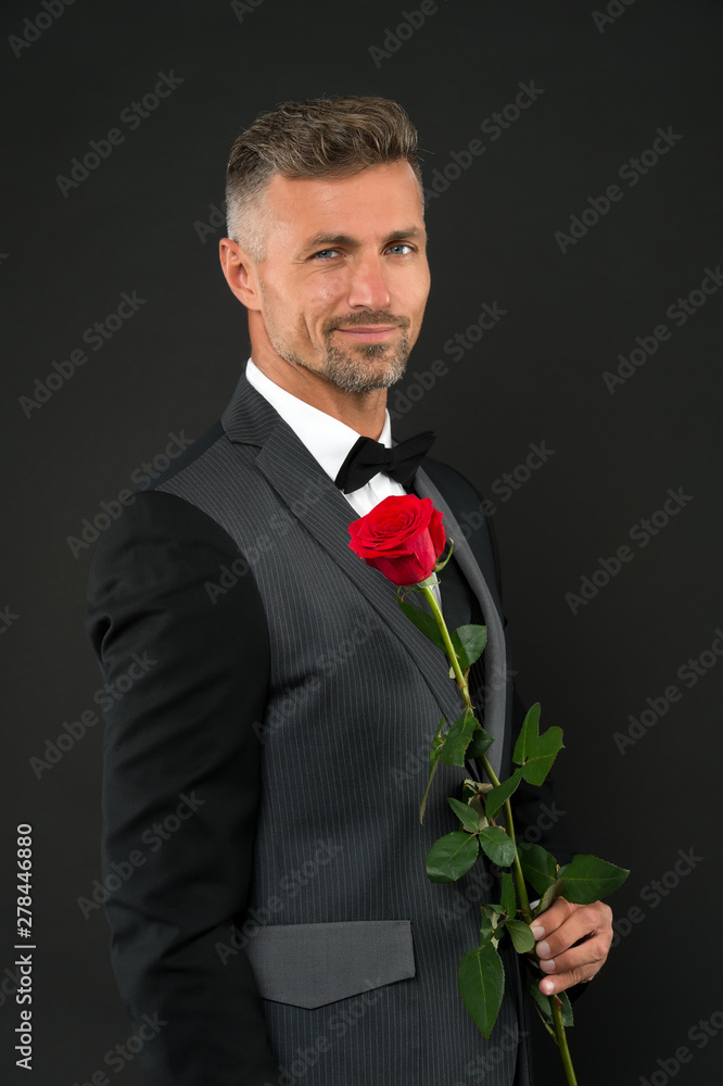 Happy womens day. Elegant man holding red rose on womes day. Handsome man in formal suit and black bowtie celebrating womens day. March 8 or international womens day celebration Happy womens day. Elegant man holding red rose on womes day. Handsome man in formal suit and black bowtie celebrating womens day. March 8 or international womens day celebration