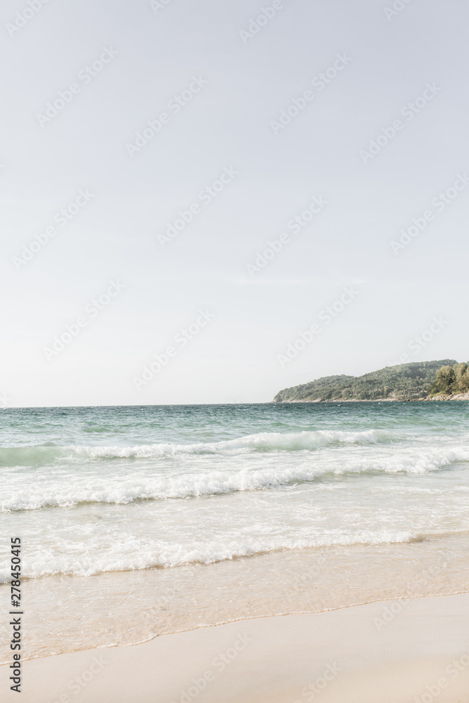 Fototapeta Beautiful tropical beach view with white sand, blue sea with waves and green island on the horizon on Phuket, Thailand. Minimal composition with neutral colors. Summer concept. Natural background.