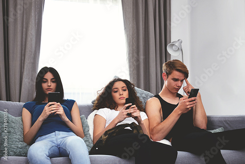 three young bored people, no party, no fun, teenagers at home, sitting and watching at smart phone, millennial generation 