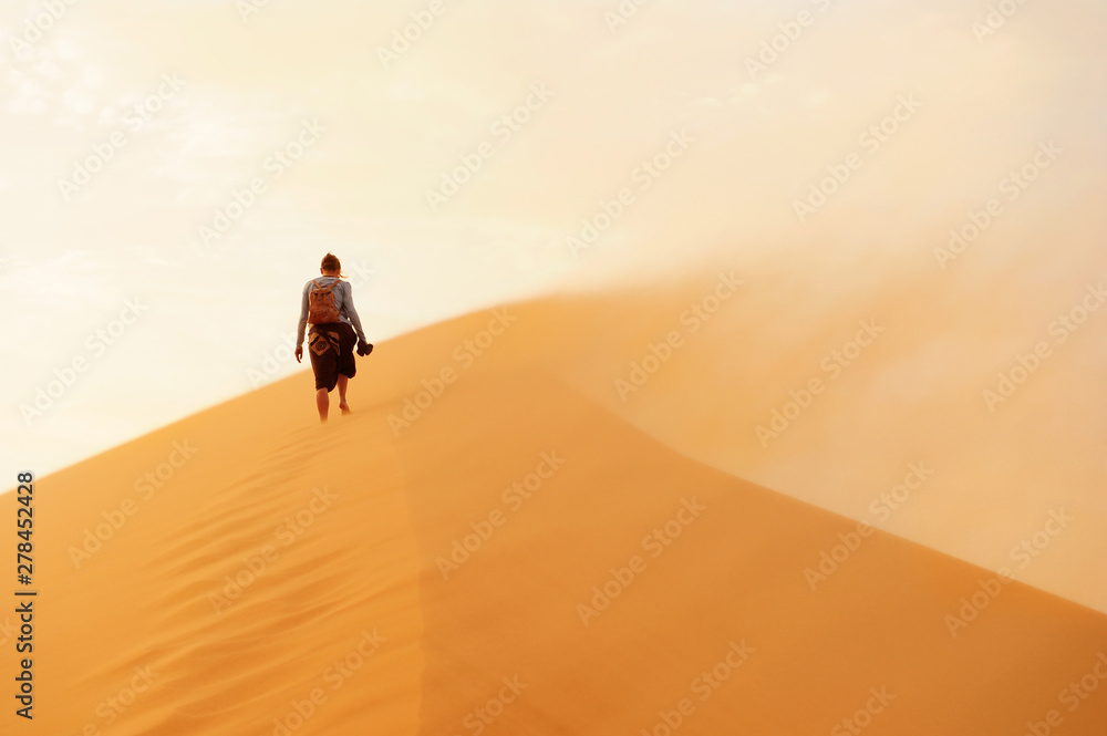 Young girl walking in sand dunes in Morocco, desert landscape, sand texture, panorama view of sunset over Sahara Young girl walking in sand dunes in Morocco, desert landscape, sand texture, panorama view of sunset over Sahara