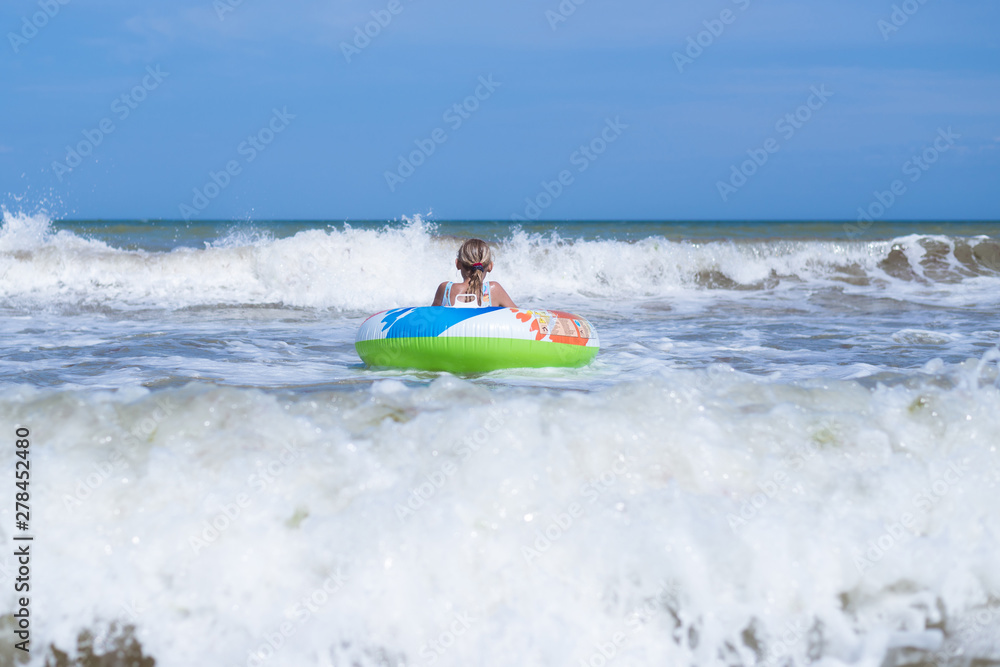 Girl teenager on an inflatable circle in the sea, ocean. Swim during the waves.