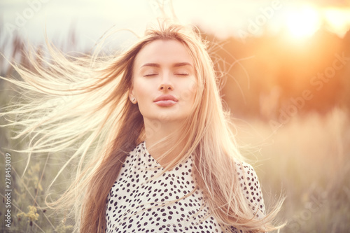 Portrait of beauty girl with fluttering white hair enjoying nature outdoors. Flying blonde hair on the wind. Beautiful young woman face closeup