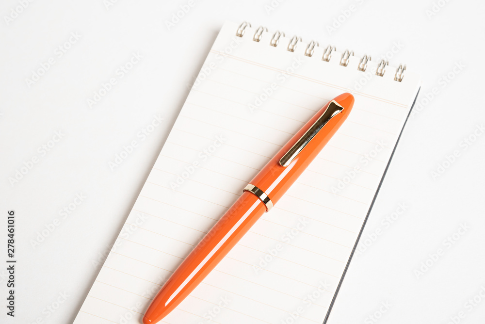 A shiny orange fountain pen together with a spiral-bound notebook. A shiny orange fountain pen together with a spiral-bound notebook.