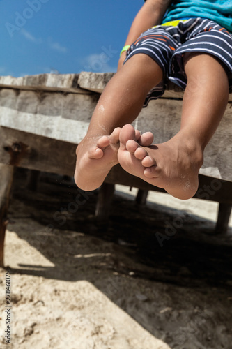 Little boy in shorts sitting on the beach with barefoot