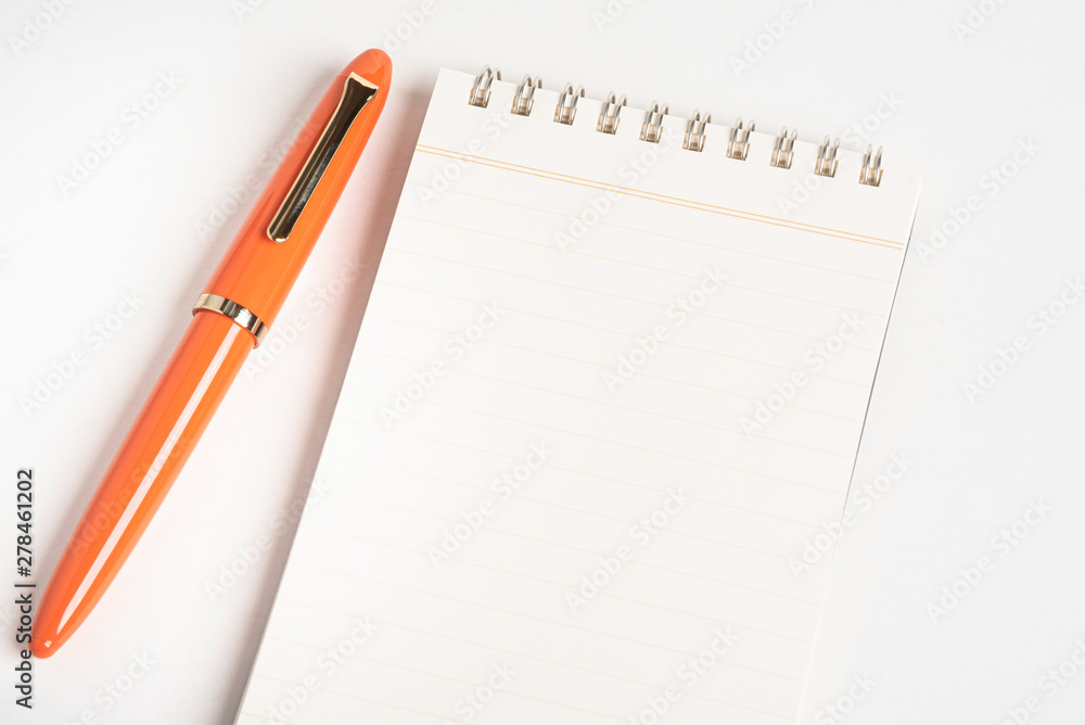 A shiny orange fountain pen together with a spiral-bound notebook. A shiny orange fountain pen together with a spiral-bound notebook.