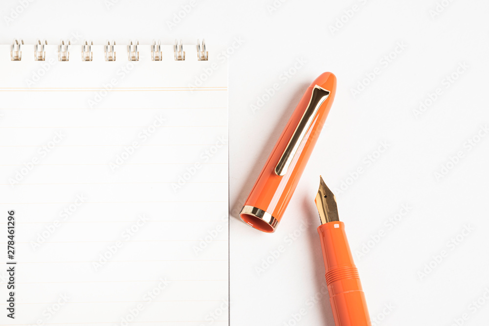 A shiny orange fountain pen together with a spiral-bound notebook. A shiny orange fountain pen together with a spiral-bound notebook.