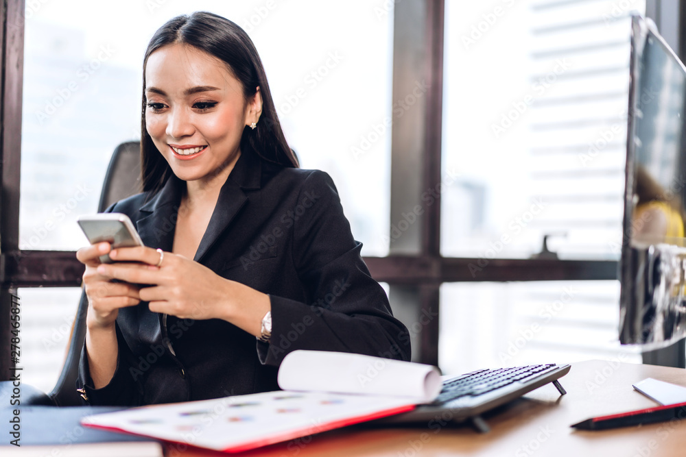 Businesswoman in elegant black suit working and use smartphone with computer sitting at table in office Businesswoman in elegant black suit working and use smartphone with computer sitting at table in office