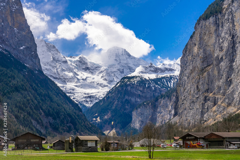 Green fields and famous touristic town with high waterfall in background, Lauterbrunnen, Bernese Oberland, Switzerland, Europe
