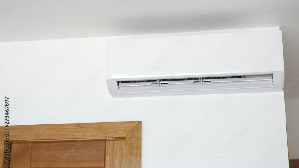 Flat air conditioner on white wall in room interior. Man pushing button on remote. Setting temperature Flat air conditioner on white wall in room interior. Man pushing button on remote. Setting temperature
