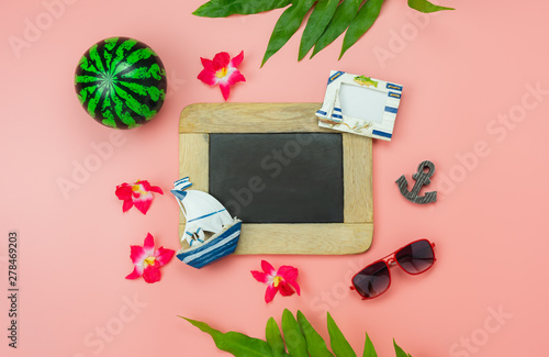 Table top view accessory plan to travel beach in summer holiday background concept.Flat lay  palm leaf with many essential items flower & palm leaf on pink paper.Blackboard for creative design text.