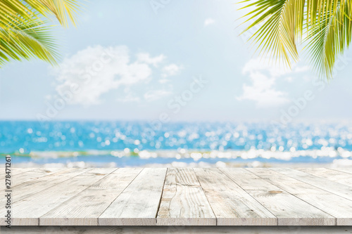 Photo Top of wood table with seascape and palm leaves, blur bokeh light of calm sea and sky at tropical beach background