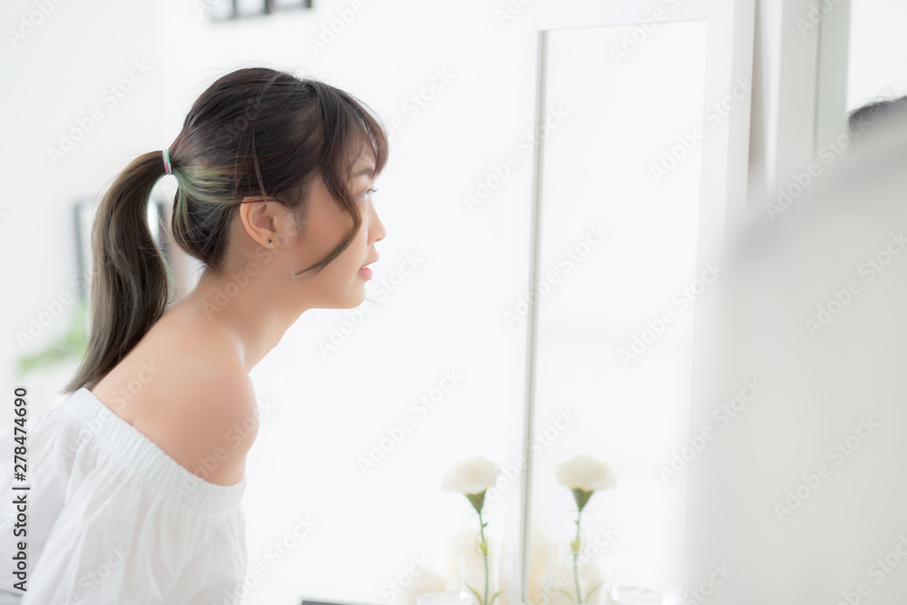 Beauty portrait young asian woman smiling look at mirror of checking skin care caucasian with wellness in the bedroom, beautiful girl happy touching face in reflection for health, lifestyle concept. Beauty portrait young asian woman smiling look at mirror of checking skin care caucasian with wellness in the bedroom, beautiful girl happy touching face in reflection for health, lifestyle concept.