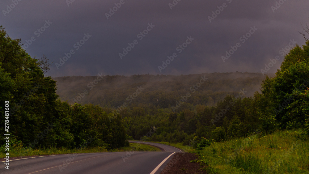 Wet asphalt after rain. Thick rain clouds. The road along the forest. Ural Mountains in rainy summer weather
