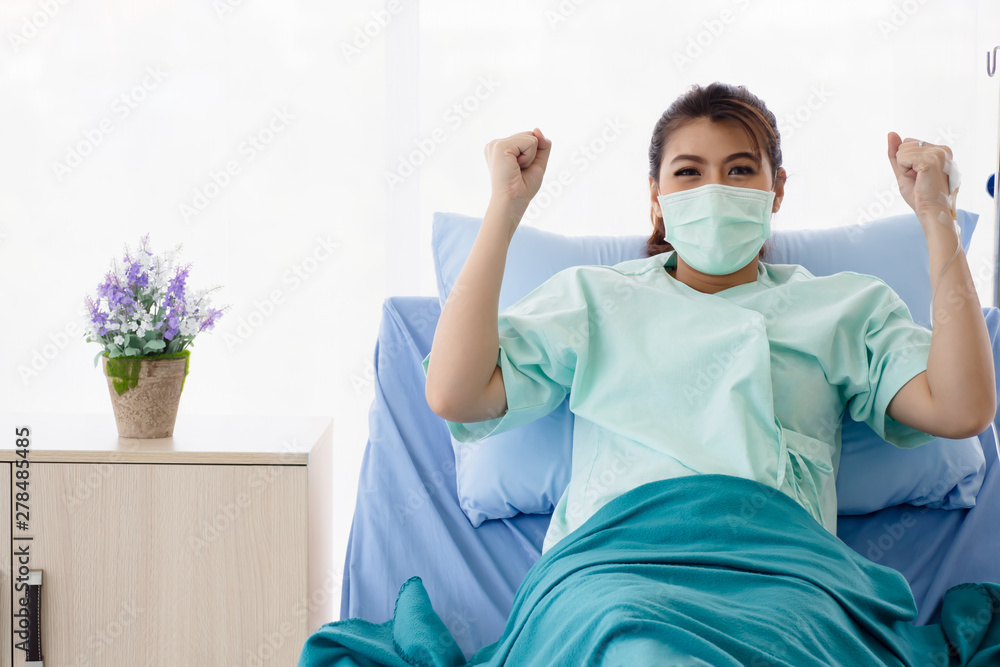 Asian women patient sitting on hospital bed and raises her arms. The young woman recover from illness. Healthcare and medical concept. Asian women patient sitting on hospital bed and raises her arms. The young woman recover from illness. Healthcare and medical concept.