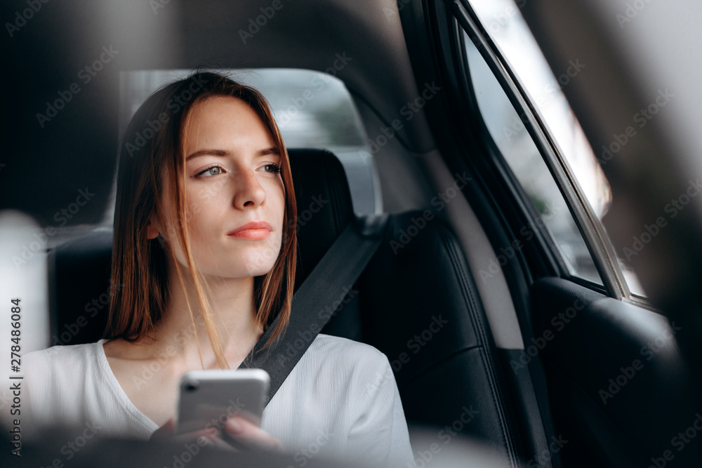 Serious young woman with a  smartphone sitting in the car and  look out