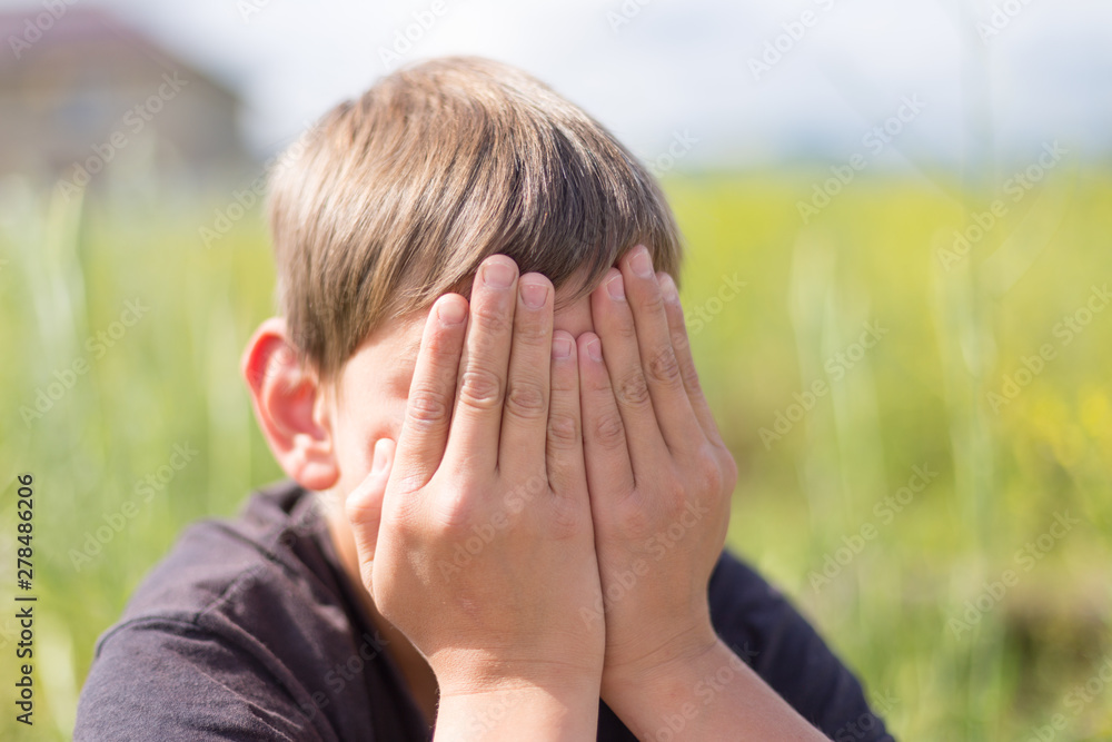 A boy in nature covers his face with his hands