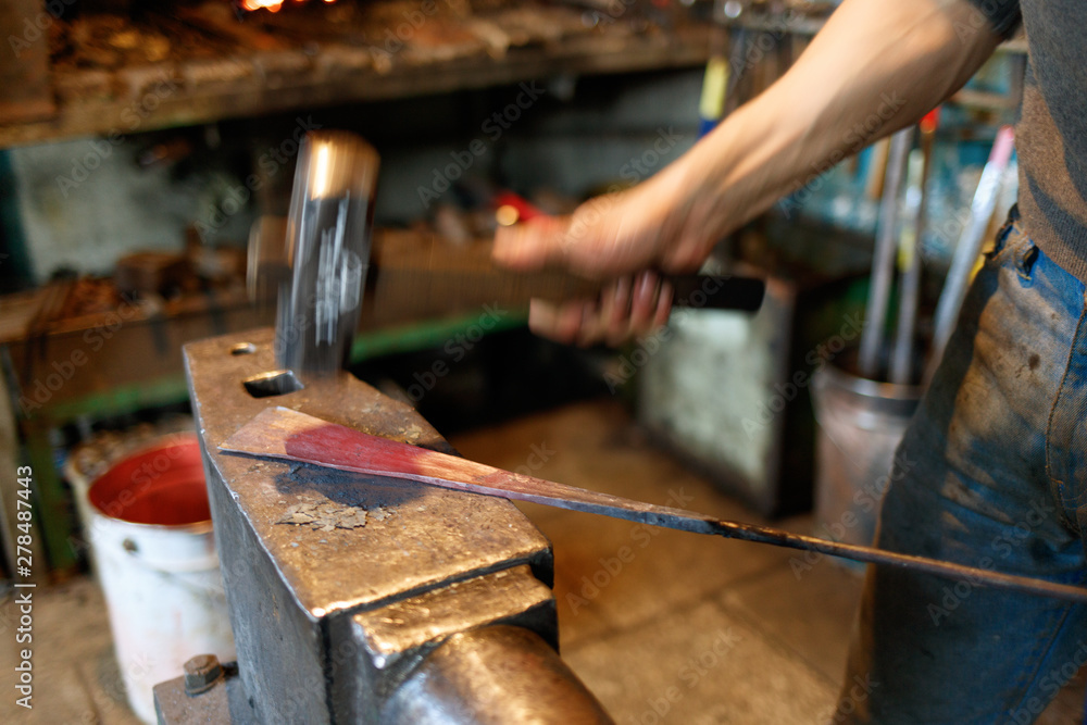 Blacksmith forging red-hot metal with hammer.