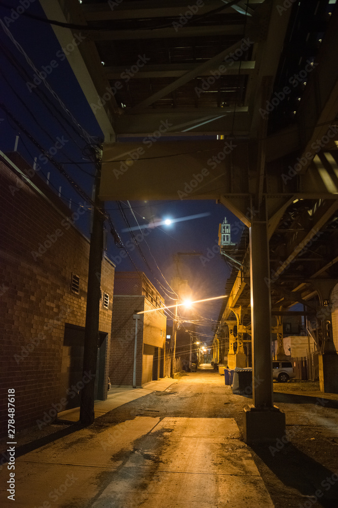 Dark and eerie Chicago urban city alley night scenery with vintage elevated CTA train tracks