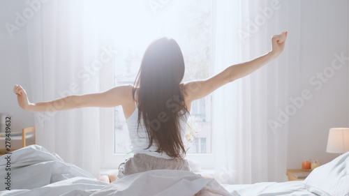 Фотография Beautiful Brunette is Waking up in the Morning, Stretches in the Bed, Sun Shines on Her From the Big Window
