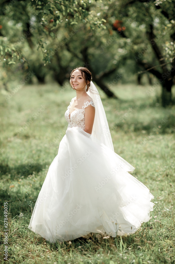 bride posing in a green park; girl in a white dress on a background of green